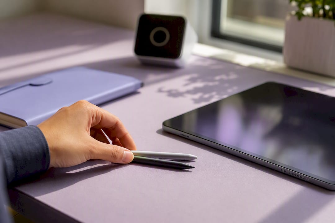 Hand adjusting digital stylus near tablet in workspace